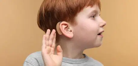 Child with a hearing aid holding their hand by their ear to hear more clearly