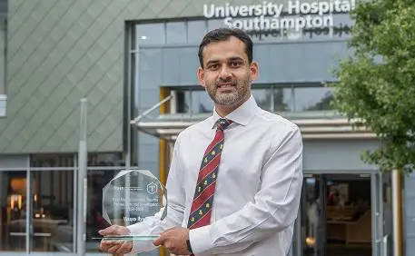 Mr M. Waqas Ilyas holding his award outside entrance to University Hospital Southampton