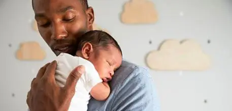Father holding his newborn baby, with clouds on the wall behind