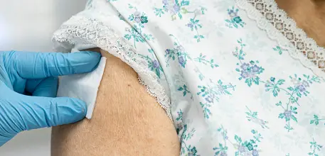 Close-up of a small bandage being held to an elderly person's arm after vaccination