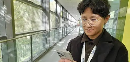 Honghui Shen looking at the app on his phone, with a long corridor stretching out behind him.