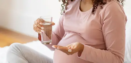 Pregnant woman shown holding a vitamin and a glass of water