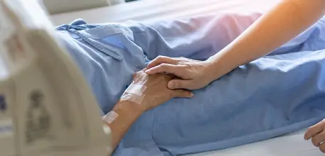 Close up of someone holding hands with patient in hospital bed