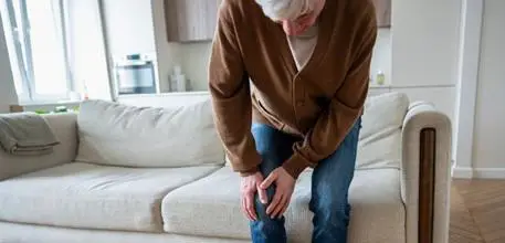 Older man getting up from a sofa, holding his knee
