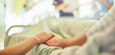 Old person holding hands in hospital bed