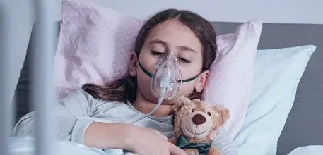 Girl in hospital bed with teddy bear and oxygen mask