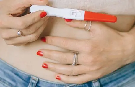 Woman holding her stomach and pregnancy test