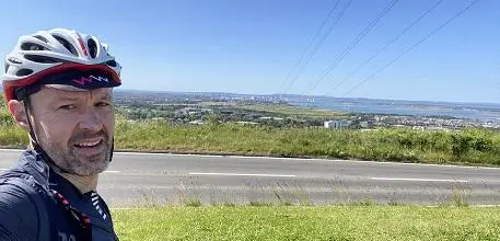 Tim Underwood in his cycling clothes and helmet next to view