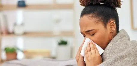 Woman wrapped in a blanket blowing her nose on a tissue