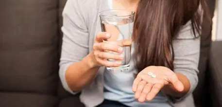 Woman taking two aspirin (white pills)