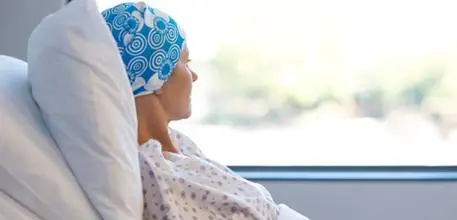 Woman with cancer in hospital bed, looking out of a window