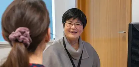 Ying Cheong at a desk talking to a woman